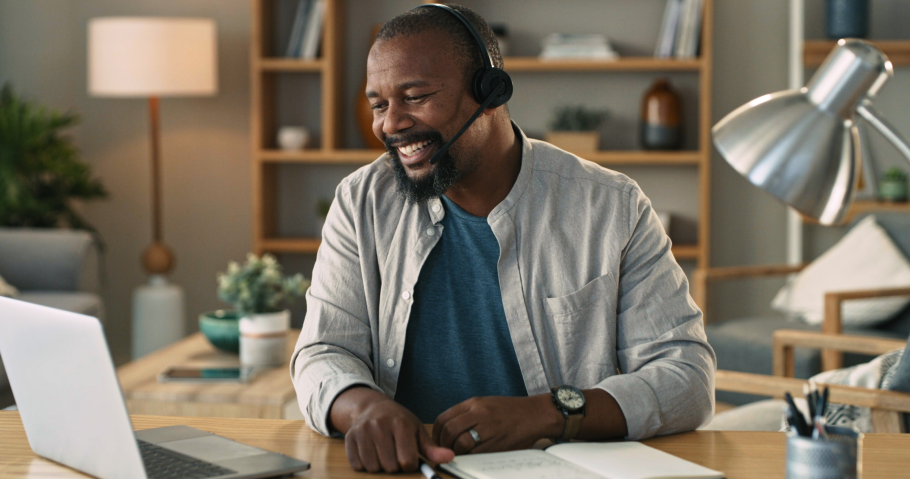 Customer care agent male working from home smiling with a headset and looking at laptop