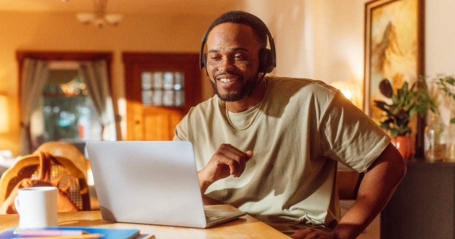 Male customer service rep in a home setting smiling at the screen with a headset on and enjoying the value of AI in CX
