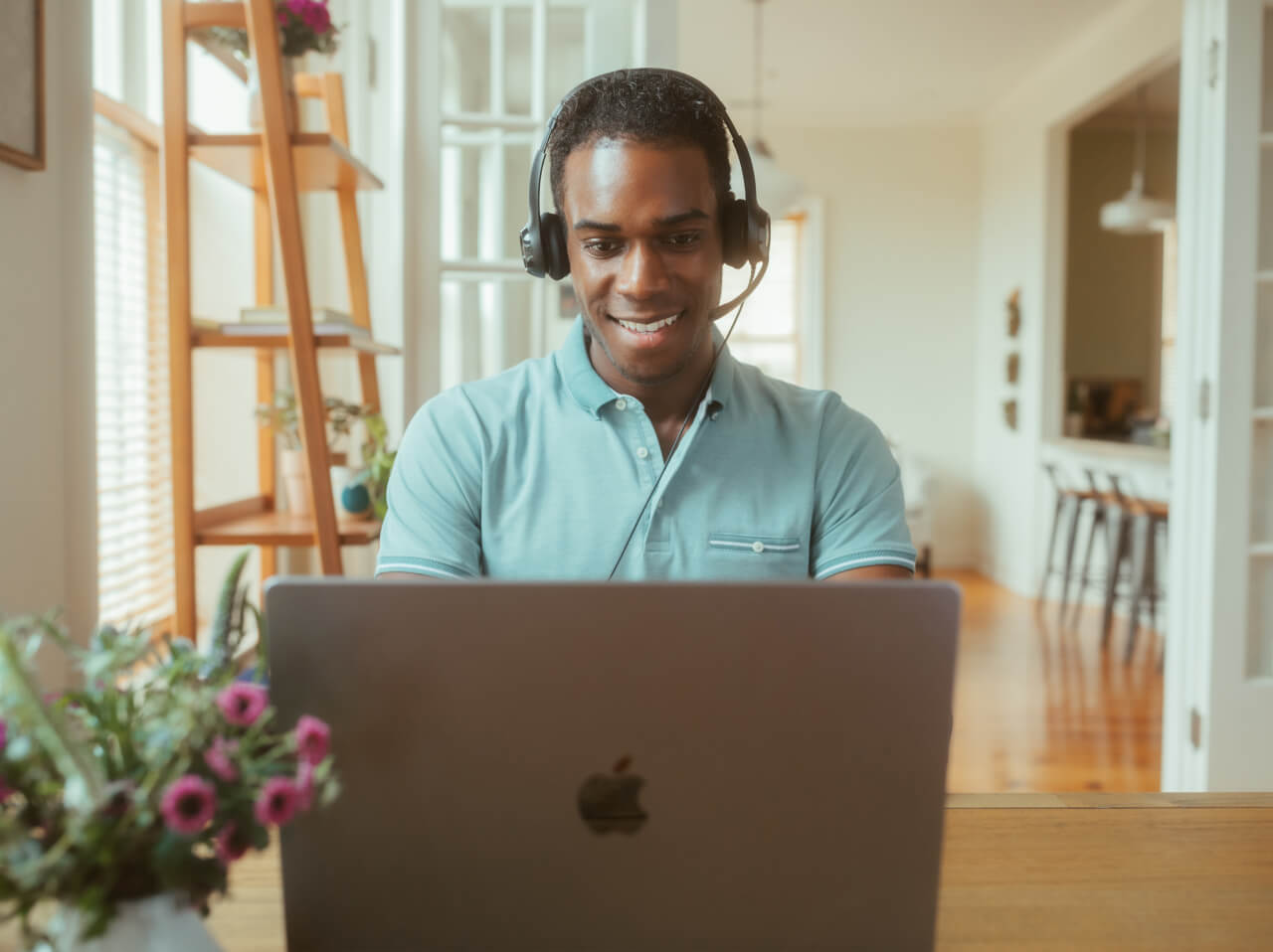 A man sitting at a desk wearing a headset, working from home, with a laptop in front of him.